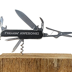 May include: A black multi-tool pocket knife with a silver blade and various tools, including a bottle opener, a corkscrew, a saw, and a pair of scissors. The knife has the words "FREAKIN' AWESOME!" engraved on the handle.