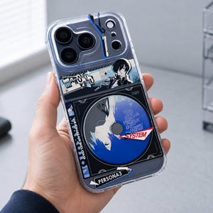 May include: A clear smartphone case featuring Persona 3 Reload graphics. The design includes a blue circular disc motif, the text "PERSONA3", "SYSTEM", and "MAKOTO YUKI", along with an illustrated character portrait. The case has a camera cutout.