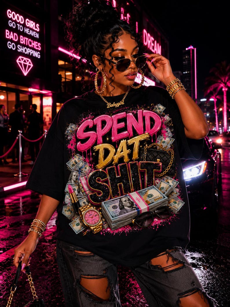 Może przedstawiać: Czarny t-shirt z kr&oacute;tkim rękawem z nadrukiem graficznym zawierającym napis SPEND DAT SHIT w kolorach r&oacute;żowym, złotym i czarnym. Wz&oacute;r zawiera obrazy stos&oacute;w studolarowych banknot&oacute;w, złotego zegarka, szminki oraz małej pikowanej torebki.
