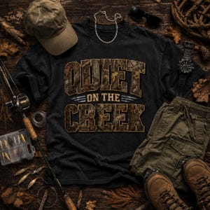Może przedstawiać: Ciemnoszary t-shirt z napisem QUIET ON THE CREEK we wzór moro, w towarzystwie beżowej czapki z daszkiem, oliwkowych szortów cargo, brązowych butów trekkingowych, wędki, pudełka na akcesoria wędkarskie, srebrnego łańcuszka i czarnego zegarka.
