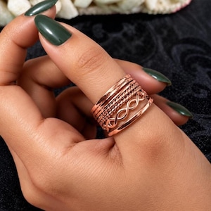 Op de afbeelding: Een ringenset in roségoudkleur bestaande uit vijf individuele ringen die samen worden gedragen. De set bevat een combinatie van gladde gepolijste ringen, een ring met een gedraaide touwstructuur en een ring met een oneindigheidssymbool.