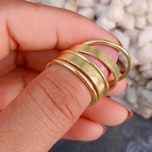 May include: A set of four gold-colored rings with varying band widths, including one thin rounded band and three wider flat bands, stacked together. The rings feature a smooth, metallic finish and are displayed in a simple, uniform design.