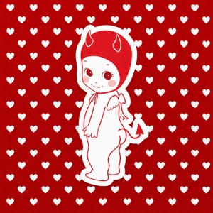 Puede incluir: Una pegatina con una figura de bebé de dibujos animados que lleva una capucha de diablo roja con cuernos, pequeñas alas blancas y una cola de diablo roja. La figura tiene mejillas sonrosadas sobre un fondo rojo con pequeños corazones blancos.