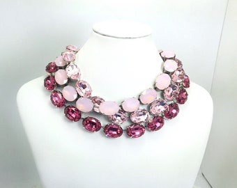 May include: A multi-layered pink and white crystal necklace with oval-shaped stones. The necklace is made of silver-toned metal and features a gradient of pink shades.