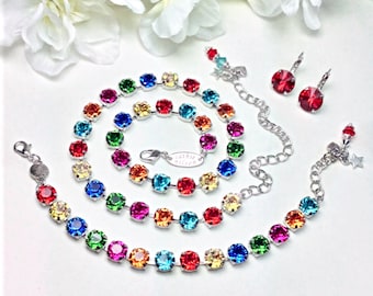 May include: A rainbow crystal necklace, bracelet and earrings set. The necklace and bracelet feature alternating rainbow coloured crystals on a silver chain. The earrings are silver with a single red crystal.