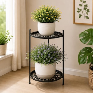 May include: A two-tier black metal plant stand with a circular frame and decorative lattice shelves. The stand holds two white ribbed ceramic pots, one containing yellow flowers and the other containing purple flowers with green foliage.
