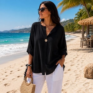 Peut inclure: Une chemise noire ample à manches trois-quarts avec un seul gros bouton au niveau de l'encolure, associée à un pantalon blanc et un sac à main en paille tressée. La chemise présente un design sans col simple et une silhouette fluide et décontractée.