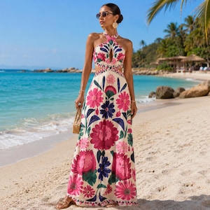 Peut inclure: Une robe longue dos nu à encolure américaine, dotée d'une base crème ornée d'un motif floral vibrant dans des tons magenta, bleu foncé et vert. La robe présente une découpe sur la poitrine, un corsage ajusté et une jupe fluide à volants.
