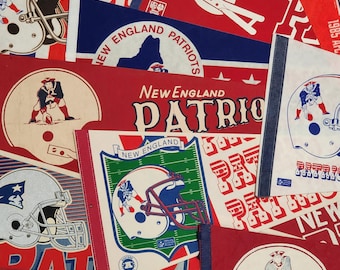 May include: A collection of vintage New England Patriots felt pennants featuring various team logos, football helmet graphics, and text including New England Patriots, all rendered in red, white, blue, and green color schemes on triangular banners.