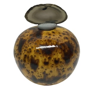 May include: A spherical object with a glossy, polished finish featuring a mottled pattern of dark brown and tan spots. A small, smooth gray stone sits atop the sphere, supporting a thin, translucent, circular slice of gray and white agate stone.