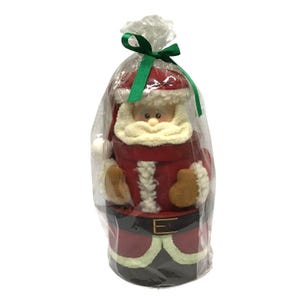 May include: A cylindrical Santa Claus figurine crafted from wood, featuring a red hat, white textured beard, and a black belt with a gold buckle. The figure is encased in a clear plastic bag tied at the top with a green satin ribbon.