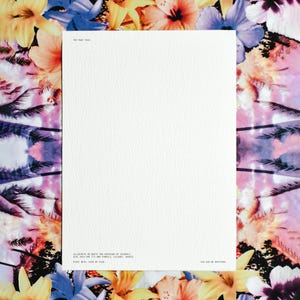 May include: A rectangular white paper sheet with a textured surface, framed by a vibrant floral and palm tree border. The text reads: THE MANY YOUS. ILLUSTRATE OR WRITE TWO VERSIONS OF YOURSELF. GIVE EACH ONE ITS OWN SYMBOLS, COLOURS, SHAPES. PAINT BOTH, SIDE BY SIDE. YOU CAN BE ANYTHING.