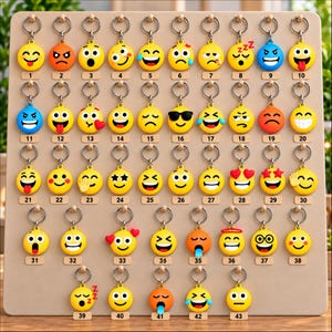Può includere: Un pannello espositivo con quarantatré portachiavi circolari, ognuno dei quali mostra un'emoji diversa. I portachiavi sono disposti in righe e colonne, con ogni articolo etichettato con un numero corrispondente da uno a quarantatré.