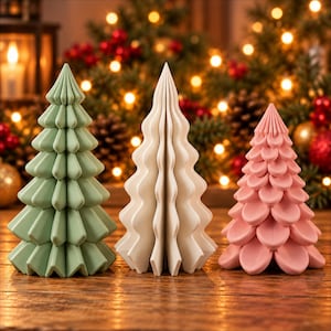 May include: Three decorative tabletop trees in a row. The left tree is sage green with a pleated, angular design. The center tree is white with a smooth, wavy, accordion-folded structure. The right tree is dusty pink with rounded, petal-like layers.