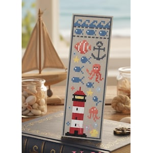 Puede incluir: Un marcapáginas rectangular con un patrón de punto de cruz sobre un fondo gris claro. El diseño incluye olas azules, peces pequeños, un faro rojo y blanco, un ancla, un pulpo, una medusa y motivos de estrellas de mar amarillas.