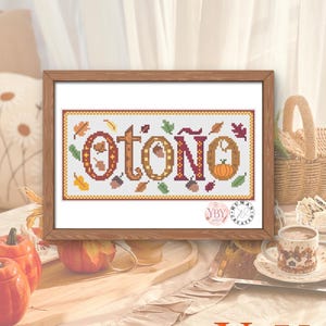 Puede incluir: Un marco de madera rectangular que contiene un patrón de punto de cruz sobre tela blanca. El diseño presenta la palabra "otoño" en letras grandes, decorativas y texturizadas, rodeadas de pequeñas hojas coloridas, bellotas y una calabaza. Un logotipo circular con el texto "YBY" es visible en la esquina inferior derecha de la tela.