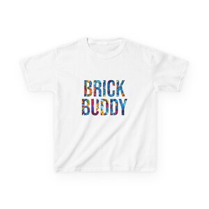 May include: A white short-sleeved t-shirt featuring the text BRICK BUDDY printed in the center. The letters are filled with a colorful, multi-patterned design consisting of small, vibrant shapes in shades of blue, red, yellow, and orange.
