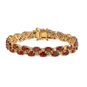 Puede incluir: Una pulsera de tono dorado con una doble hilera de granates rojos de corte ovalado que se alternan con pequeñas piedras blancas transparentes. La pieza incluye un cierre de caja seguro con un patrón de filigrana decorativo en los eslabones.