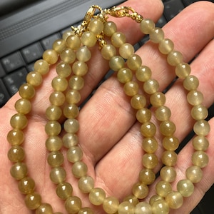 May include: A beaded bracelet featuring smooth, round, translucent golden-brown gemstone beads strung together. The bracelet is finished with a polished gold-tone metal lobster claw clasp and small gold-tone spacer beads at the closure point.