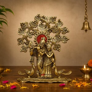 May include: A brass statue of Radha and Krishna standing under a tree, with Krishna playing a flute. The figures are flanked by two peacocks on a base, featuring a circular red accent behind their heads, crafted with intricate metal detailing.
