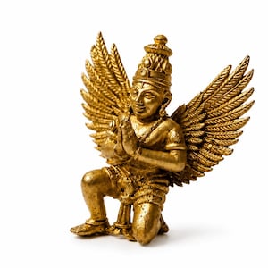 May include: A gold-coloured statue of a winged figure kneeling with hands pressed together in a prayer position. The figure features detailed feathered wings, a pointed headdress, and ornate jewellery, all rendered in a metallic gold finish.