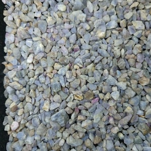 Peut inclure: Une collection de petits fragments de pierres précieuses brutes et polies dans des tons bleu clair, gris pâle et lavande doux, avec des éclats occasionnels de jaune sourd et de rouge rosé dispersés dans cet amas de pierres granuleuses.
