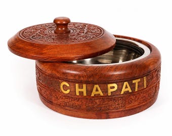 Puede incluir: Un recipiente redondo de madera con tapa extraíble, que presenta intrincadas tallas florales y la palabra CHAPATI en letras de metal de color dorado en el lateral. El interior está revestido con un inserto circular de acero inoxidable.
