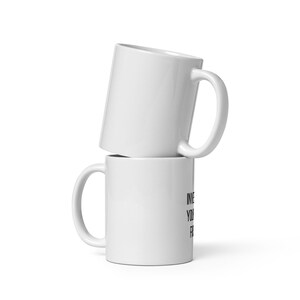 May include: Two stacked white ceramic mugs with a glossy finish. The bottom mug features black printed text on its side that reads INVEST IN YOUR FUTURE. Each mug has a curved handle on the right side and a smooth, cylindrical body design.
