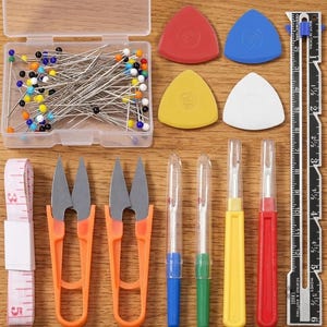 May include: A sewing kit containing a clear plastic box of multi-colored straight pins, four triangular tailor's chalk pieces in red, blue, yellow, and white, two orange thread snips, four seam rippers, a measuring tape, and a 6-inch metal ruler.