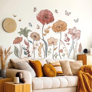 May include: A wall decal set featuring a collection of illustrated flowers in shades of dusty pink, muted orange, and sage green, accompanied by small butterflies and bees. The floral arrangement includes various stems, leaves, and blossoms.