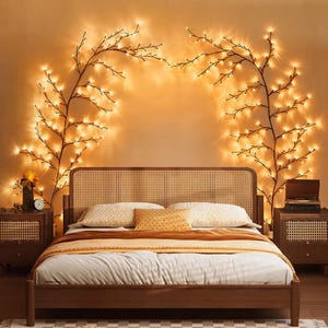 May include: A wooden bed frame with a woven cane headboard, positioned between two matching wooden nightstands with cane detailing. Two arched, dark-colored branch-shaped light fixtures with warm glowing LED bulbs are mounted on the wall.