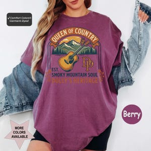 K&ouml;nnte beinhalten: Ein beerenfarbenes T-Shirt mit Rundhalsausschnitt und einem Grafikdruck einer akustischen Gitarre, Bergen und einem Schmetterling. Der Text lautet QUEEN OF COUNTRY, EST. SMOKY MOUNTAIN SOUL, DOLLY'S HERITAGE und DP. Comfort Colors Kleidungsst&uuml;ck.
