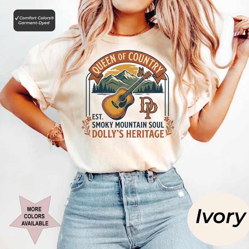 K&ouml;nnte beinhalten: Ein elfenbeinfarbenes T-Shirt mit einem Grafikdruck, der eine braune Akustikgitarre, gr&uuml;ne Berge und einen Schmetterling zeigt. Der Text lautet: QUEEN OF COUNTRY, EST. SMOKY MOUNTAIN SOUL, DOLLY'S HERITAGE und DP. Comfort Colors st&uuml;ckgef&auml;rbtes T-Shirt.