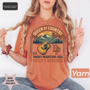 K&ouml;nnte beinhalten: Ein yam-farbenes Kurzarm-T-Shirt mit einer Grafik aus Akustikgitarre, Bergen und einem Schmetterling. Der Text lautet Queen of Country, Est. Smoky Mountain Soul und Dolly's Heritage. Ein Comfort Colors Garment-Dyed Etikett ist zu sehen.