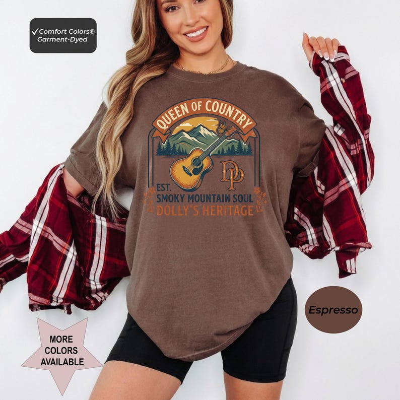 K&ouml;nnte beinhalten: Ein espressofarbenes Kurzarm-T-Shirt mit einem Grafikdruck einer akustischen Gitarre, Bergen und einem Schmetterling. Der Text lautet Queen of Country, Est. Smoky Mountain Soul und Dolly's Heritage. Ein rot-wei&szlig; kariertes Hemd ist dar&uuml;ber geschichtet.