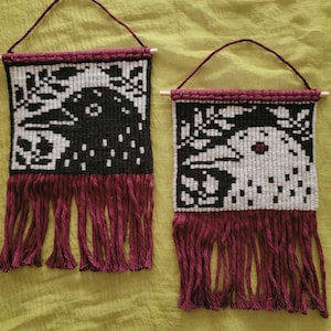 May include: Two rectangular woven wall hangings featuring bird profiles. One displays a black bird on a white background, the other a white bird on a black background. Both have maroon fringe, maroon hanging cords, and wooden dowels at the top.