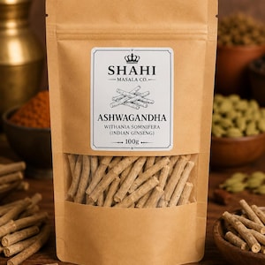 K&ouml;nnte beinhalten: Ein wiederverschlie&szlig;barer Beutel aus beigem Kraftpapier mit Ashwagandha-Wurzeln. Das wei&szlig;e Etikett tr&auml;gt den Text SHAHI MASALA CO., ASHWAGANDHA, WITHANIA SOMNIFERA (INDIAN GINSENG) und 100g. Ein Sichtfenster zeigt die hellbraunen Wurzelst&uuml;cke.