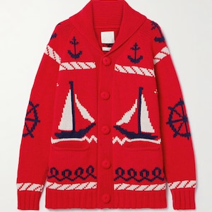 May include: A bright red knit cardigan featuring a shawl collar, long sleeves, and a button-front closure. The sweater is decorated with a nautical pattern in navy blue and white, including sailboats, anchors, ship wheels, and rope motifs.