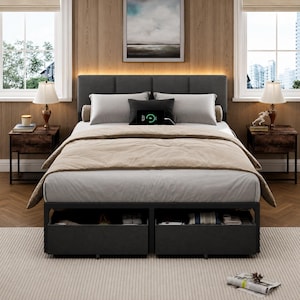 May include: A platform bed frame with a dark gray upholstered headboard and two integrated storage drawers at the base. The bed is dressed in a light gray sheet and a beige comforter, featuring a black digital charging pad on the pillows.