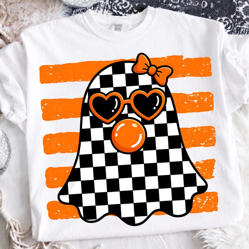 Pode incluir: Uma t-shirt branca com um gr&aacute;fico de um fantasma com padr&atilde;o xadrez preto e branco. O fantasma usa &oacute;culos de sol laranja em forma de cora&ccedil;&atilde;o, um la&ccedil;o laranja na cabe&ccedil;a e tem uma bolha laranja &agrave; frente do rosto, sobre riscas cor de laranja.