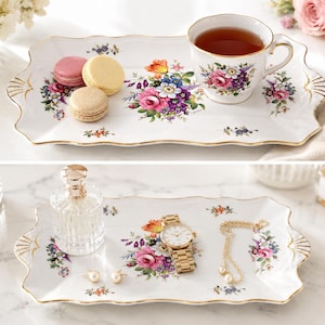 Op de afbeelding: Een rechthoekig wit porseleinen dienblad met geschulpte randen en een gouden rand, voorzien van een kleurrijk bloemenpatroon. De bovenste afbeelding toont het dienblad met een theekopje en drie macarons. De onderste afbeelding toont het dienblad met een parfumflesje, een gouden horloge, een gouden ketting en twee pareloorbellen.