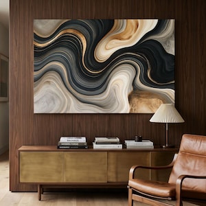May include: A large rectangular wall art piece featuring abstract swirling patterns in shades of black, charcoal, cream, and metallic gold. The artwork is displayed above a wooden sideboard with brass doors and a pleated table lamp.