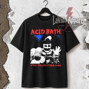 Peut inclure: Un t-shirt noir à manches courtes avec une impression graphique représentant un clown tenant des ballons. Le texte ACID BATH apparaît en rouge au-dessus du clown, et le texte WHEN THE KITE STRING POPS en rouge en dessous. Logo en haut à droite.