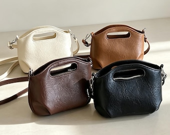 May include: Four small handbags with a textured finish, each featuring a top handle cutout and a detachable shoulder strap. The bags are available in cream, tan, dark brown, and black, and each includes a top zipper closure with silver hardware.