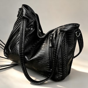 May include: A black handbag with a textured crocodile skin pattern, featuring two vertical zippered pockets on the front, braided side detailing, and two shoulder straps. The bag includes silver-toned metal hardware and a top zipper closure.