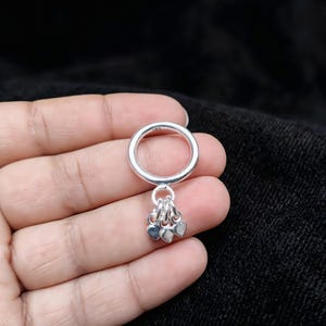 Puede incluir: Un anillo de plata que presenta una banda circular lisa con un sello de contraste. Tres pequeños dijes de plata pulida en forma de corazón cuelgan de la parte inferior de la banda mediante anillas individuales, creando un efecto colgante.