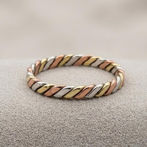 May include: A tri-color ring featuring a twisted rope design. The band is constructed from alternating segments of polished yellow gold, rose gold, and silver-toned metal, creating a continuous braided pattern around the entire circumference.