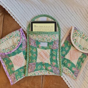 May include: Three quilted fabric book covers in green, purple, and pink with floral patterns. The middle cover has a book inside with the text "Mystery Blessing, tells her son, Luke. There's an envelope in the third drawer of the desk. Do the key. The mother nods. They will unlock the box. The mother's cottage old"