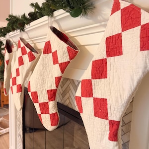 May include: A set of four quilted Christmas stockings featuring a red and white checkered pattern. Each stocking is constructed with a textured, stitched fabric design and includes a plaid fabric lining visible at the top opening of the stockings.