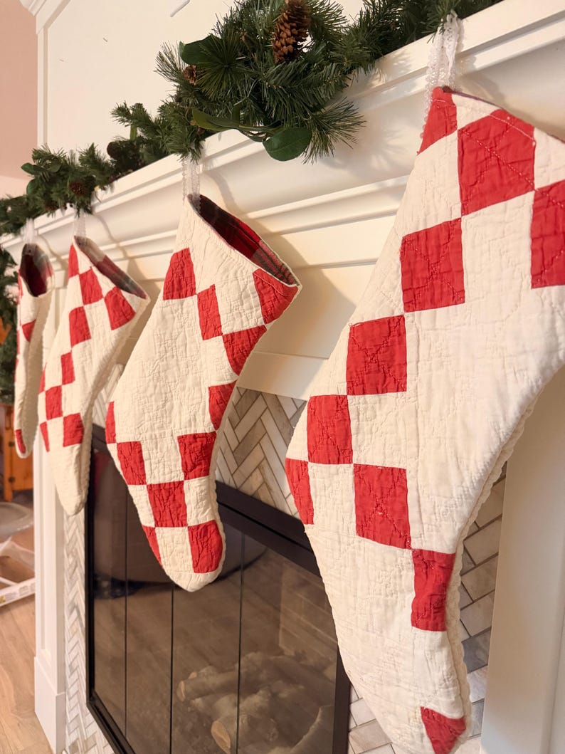 May include: A set of four quilted Christmas stockings featuring a red and white checkered pattern. Each stocking is constructed with a textured, stitched fabric design and includes a plaid fabric lining visible at the top opening of the stockings.